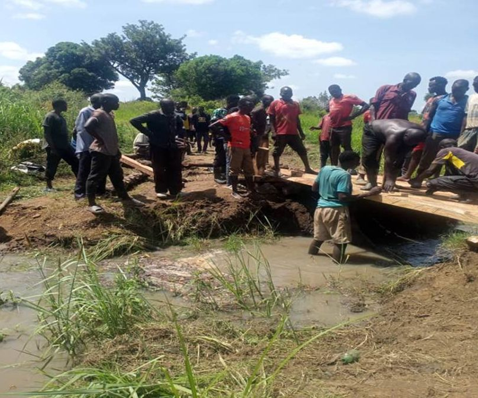 Large group of Community Members working on constructing a wooden bridge over a river.